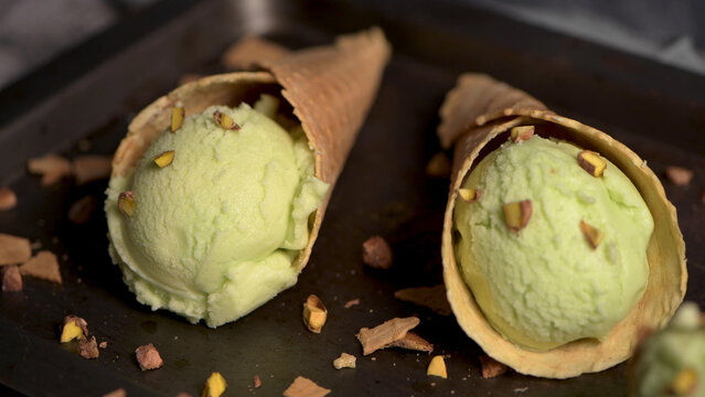 Pistachio Ice Cream Scoops in Waffle Cones on a Dark Tray