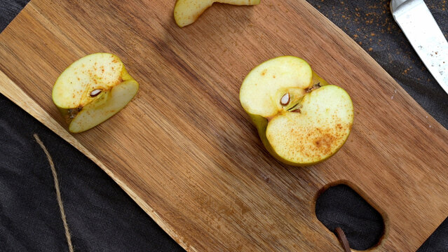 Freshly cut apple halves dusted with cinnamon powder on a wooden cutting board