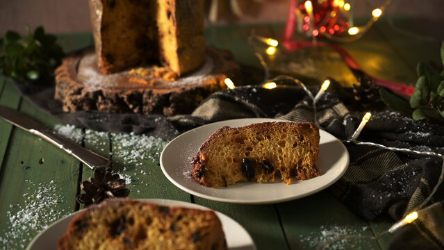 Slice of traditional Italian panettone cake served on a plate with festive holiday lights and decor