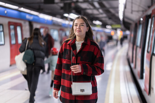Girl standing at metro stop, subway station platform, waiting for transport. She carefully reads signs and looks for required metro train departure platform.