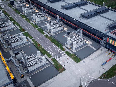 Aerial view of a modern data center facility featuring multiple HVAC cooling units on flat rooftops, paved service roads, and a large warehouse building in The Netherlands.