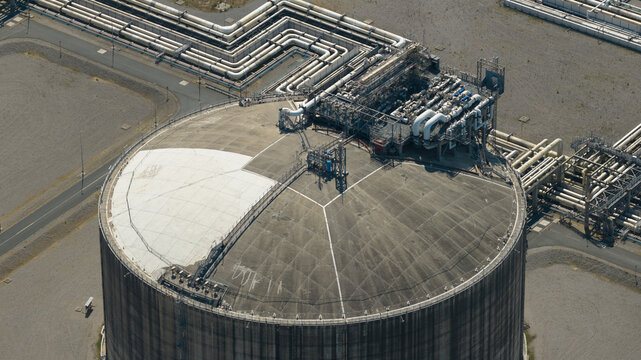 Aerial view of the Dunkirk LNG Terminal featuring a large circular storage tank with intricate piping infrastructure and industrial equipment in Loon-Plage, Hauts-de-France, France.