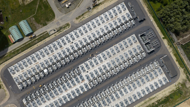 Aerial view of a large industrial energy storage facility with rows of containerized units, paved access roads, and surrounding green space in Vilvoorde, Vlaanderen, Belgium.