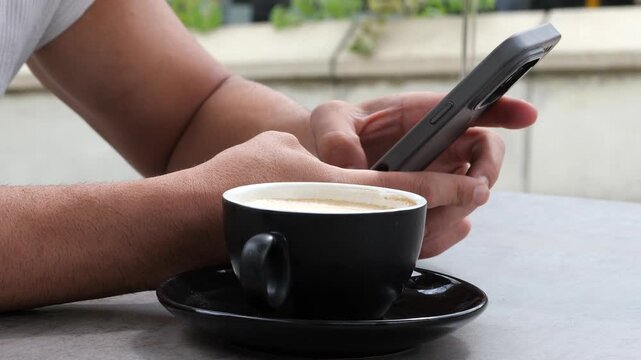 Close Up Man Hands Holding Smartphone and Texting Sitting at Outdoor Cafe Table with Hot Cappuccino Coffee Cup Urban Lifestyle Technology Concept