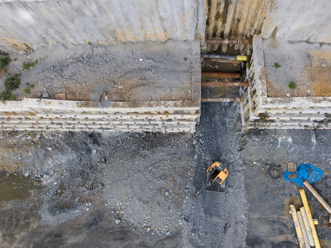 Aerial view of an excavator working at a construction site with a concrete retaining wall and exposed pipes in Istanbul, Istanbul, Turkiye.