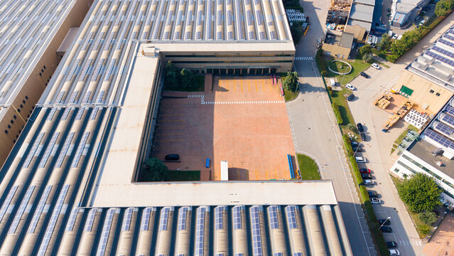 Aerial view of AKNO Settala 2 Business Park featuring large warehouse buildings with solar panel arrays, a central paved courtyard, and surrounding parking areas in Settala, Lombardia, Italy.