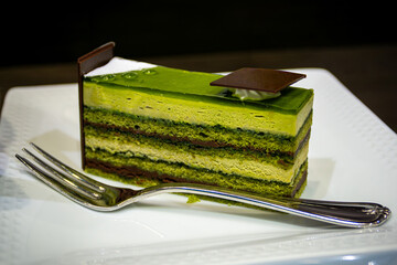 Closeup of a slice of Japanese matcha opera cake dessert with green tea layers of matcha sponge, cream, and chocolate ganache served on a plate with a fork. © ronniechua