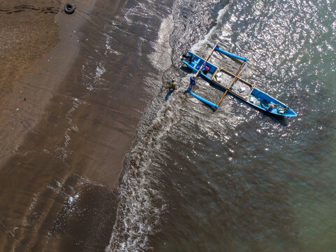Aerial view of a blue traditional fishing boat with fishermen on the sandy shore in Cilacap, Central Java, Indonesia.