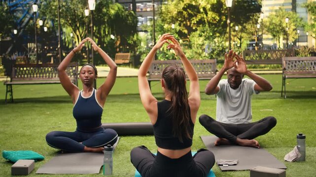 Yoga participants sit cross-legged on mats, starting outdoor meditation and deep breathing in lotus position during a calm Pilates and mindfulness practice.