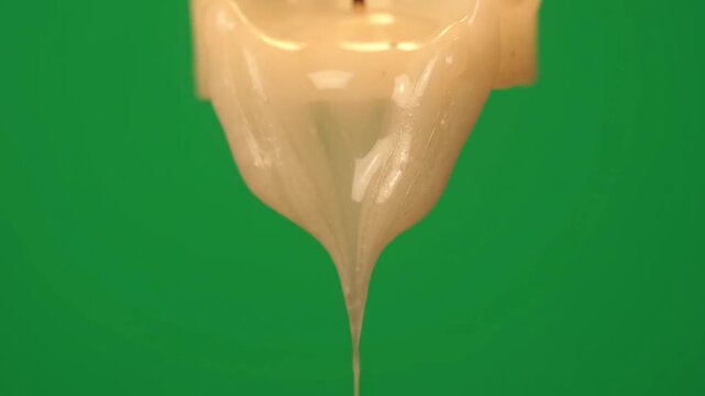 Molten white wax dripping slowly from a burning candle wick against a vibrant green surface creates an evocative scene representing passing time rituals tranquility meditation warmth and