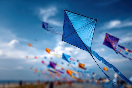 Vibrant colorful kites soaring in a bright blue sky during a lively outdoor festival on a sunny day near the coast with blurred background scenery