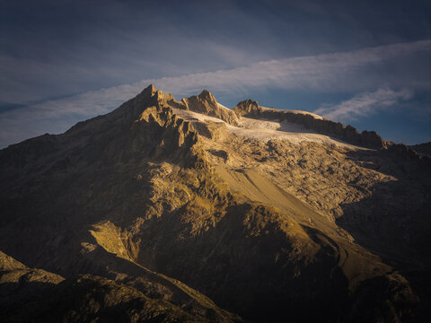 Aerial view of the Aletsch Glacier with rugged mountain peaks, icy slopes, and dramatic shadows cast by the golden hour light in Fieschertal, Valais, Switzerland.
