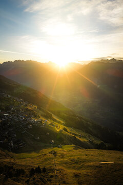 Aerial view of Aletsch Glacier at sunset with golden light illuminating the mountain slopes and the village of Fieschertal, Valais, Switzerland.