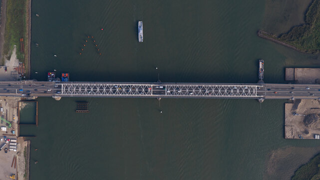 Aerial view of the Merwedebrug truss bridge spanning the river with traffic flowing across and a boat navigating the water in Gorinchem, North Brabant, Netherlands.