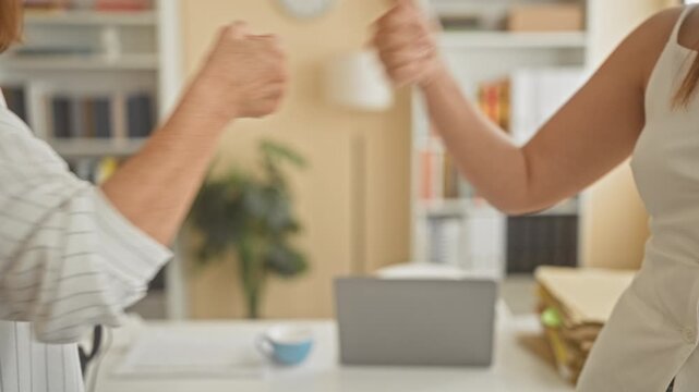 Woman clasping hands with business partner over a desk strewn with files and a laptop in an office building; collaboration trust support.