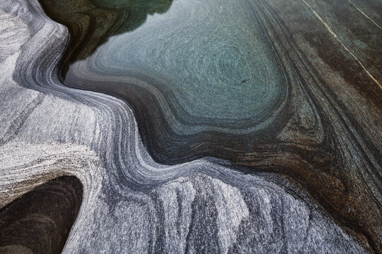 View of smooth, water-worn granite rock formations with swirling patterns and clear turquoise water in the Verzasca River in Lavertezzo, Ticino, Switzerland.