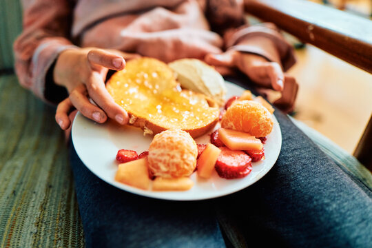 Boy Holding a Plate of Honey Toast and Fresh Fruit on a Sofa