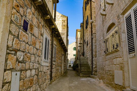 View of a narrow stone street in the historic old town of Hvar, featuring traditional Mediterranean architecture, rustic walls, and shutters in Hvar, Split-Dalmatia County, Croatia.