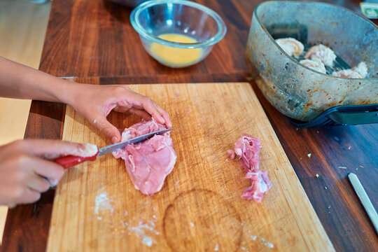 Boy Cutting Raw Chicken on a Wooden Cutting Board in a Kitchen