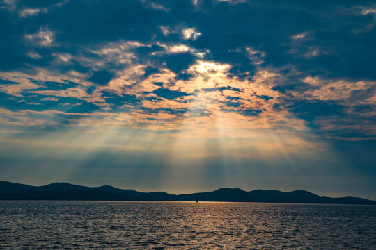 View of sun rays breaking through dramatic clouds over the Adriatic Sea with distant hills of Hvar, Split-Dalmatia County, Croatia.