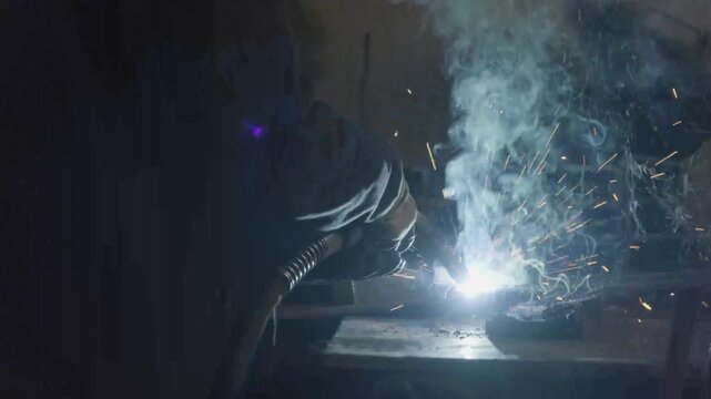 Close-up of skilled welder joining steel metal plates with bright glowing sparks in workshop