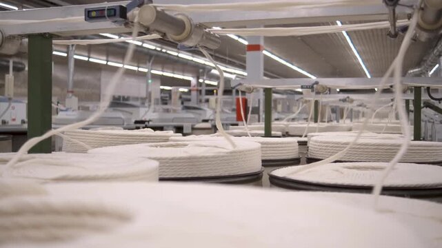 Macro detail of cotton threads feeding into modern machinery weaving fabric in textile factory