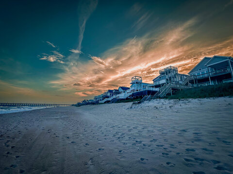 View of Topsail Island beach houses at sunset with wooden stairs leading to the sand and a pier in the distance in North Topsail Beach, North Carolina, United States.