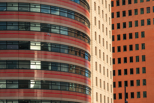 View of modern office buildings with a curved red tiled facade and an adjacent orange brick building with grid windows in Rotterdam, South Holland, Netherlands.