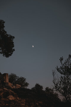 View of the moon rising over the rocky landscape and trees in Athens, Greece.