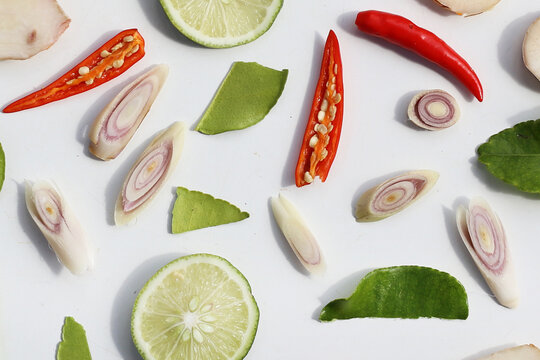 A colorful, close-up pattern of Thai herbs: lime slices, galangal, lemongrass, chilies, and kaffir lime leaves.