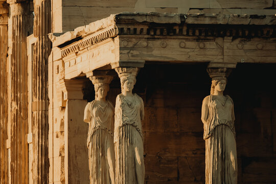 View of the Caryatids of the Erechtheion on the Acropolis with stone columns and ancient architectural details illuminated by warm golden hour sunlight in Athens, Greece.