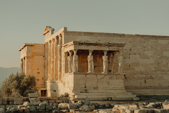 View of the Erechtheion at the Acropolis featuring the iconic Caryatid porch with marble statues of draped female figures under warm golden hour light in Athens, Greece.