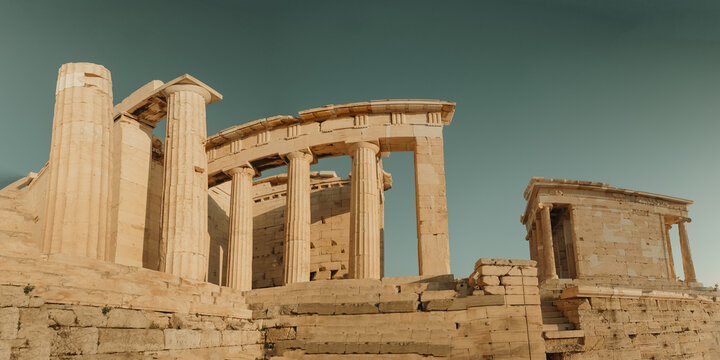 View of the ancient columns and stone structures of the Acropolis under a clear sky in Athens, Greece.