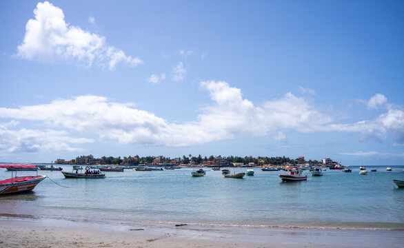 View of traditional fishing boats anchored at Petite Ngor Beach with a coastal town in the background under a clear blue sky, Dakar, Region de Dakar, Senegal.