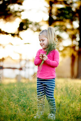 Naklejka premium Nature, child and pick grass to explore, play and development in environment on holiday. Smile, girl and kid gather plants at park for collection, learning and growth on spring vacation with bokeh