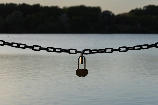 Silhouette of a love lock padlock on a chain above a lake