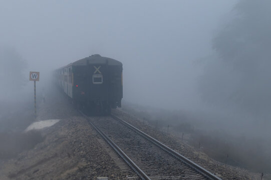 View of a train moving along the tracks through dense fog with a warning sign visible on the side in Multan City, Punjab, Pakistan.