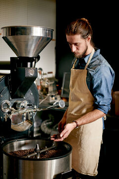 Man, coffee beans and machine in roastery for roasting, flavor enhancing or inspection for distribution. Small business, master roaster and equipment in startup for quality control in export industry