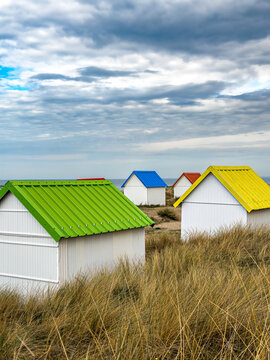 View of colorful beach huts with green, blue, red, and yellow roofs nestled in the dunes at Gouville-sur-Mer, Normandy, France.
