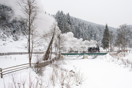 View of the Mocanita steam train crossing a bridge through a snowy forest landscape in Moldovita, Suceava County, Romania.