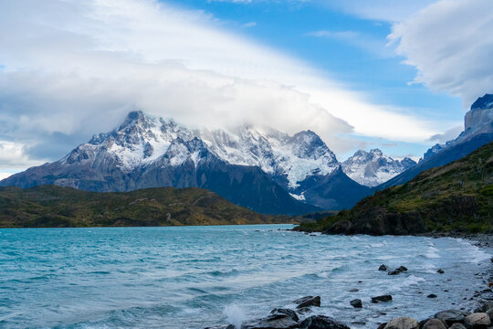 View of Cordillera del Paine with snow-capped peaks, turquoise lake, and rocky shoreline in Torres de Paine, Magallanes, Chile.