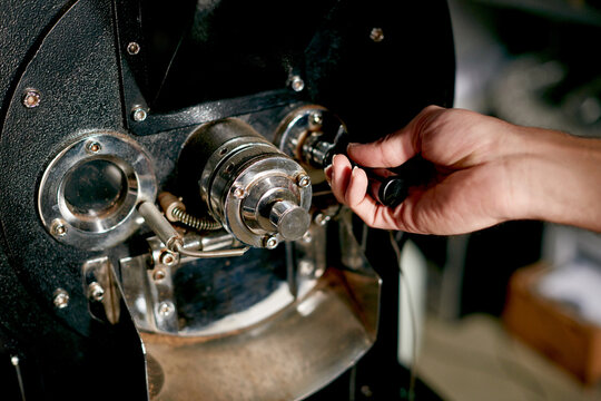 Coffee, machine and hands of person in cafe for espresso, hospitality and fresh. Caffeine roast beans, quality assurance or flavor development with closeup of employee in roastery for artisan process
