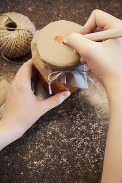 Hands decorating rustic homemade gift jar with drawn heart symbol