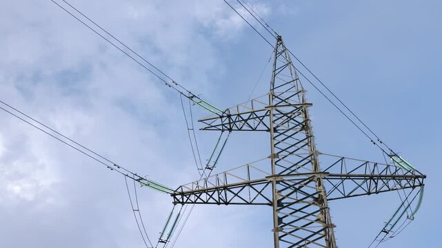 Close up view of a steel electricity transmission tower supporting multiple overhead power lines and suspended insulators against a blue sky