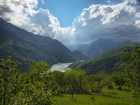 Dramatic clouds and blue sky over steep mountains and a sunlit reservoir lake, with lush green trees, a grassy slope, and a distant snowy peak.
📍 Hawraman, Sarvabad, Kurdistan 