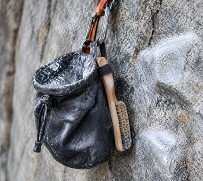 Chalk bag hanging on a granite wall with dusty mouth and a stiff brush in the loop