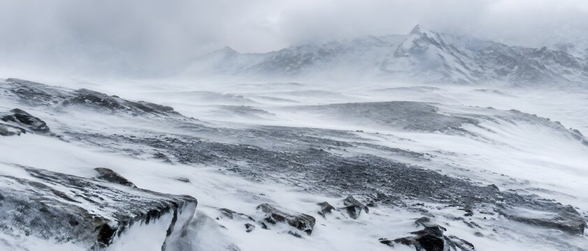Snowstorm sweeping across an alpine plateau with wind scoured gravel pans and half buried slabs