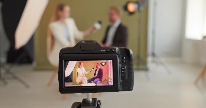 Interview journalist with guest in studio recording. Professional production setup with camera display, lights, tripod, microphone and backdrop. Concept of communication and media storytelling.