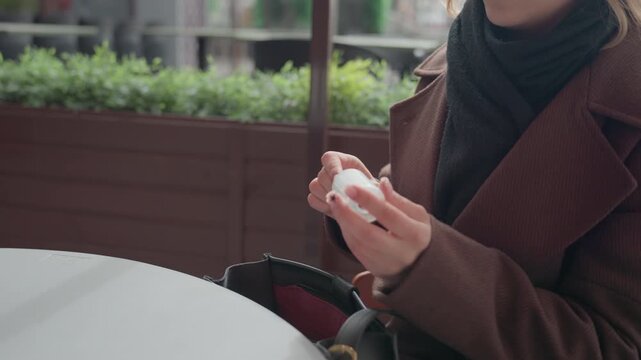 Woman wearing dark clothing handles small cleaning device at table. Woman manipulates object with hands while seated near greenery and windowed background placing item into bag