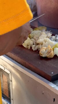Close up video of Indonesian street vendor hands chopping batagor fried dumpling tofu with cabbage and potato on wooden cutting board. Traditional street food preparation with peanut sauce